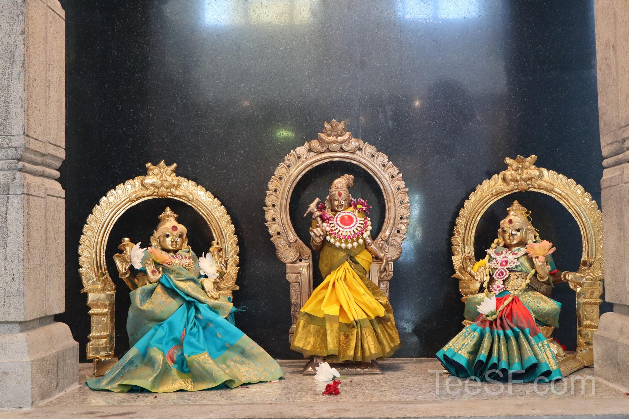 Three colorful shrine figures arranged against a dark wall.